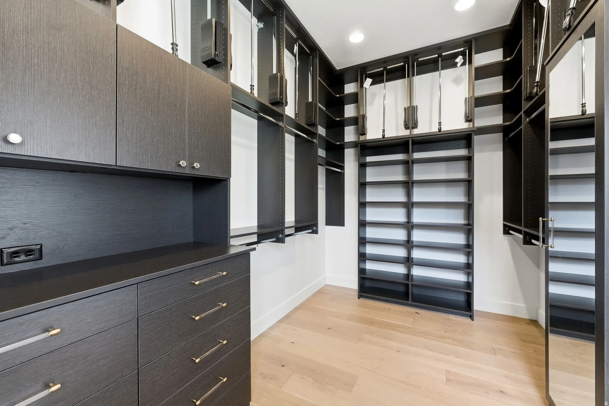 Custom closet system featuring dark wood-finish cabinetry, ample shelving, integrated drawer storage, and light wood-finish flooring