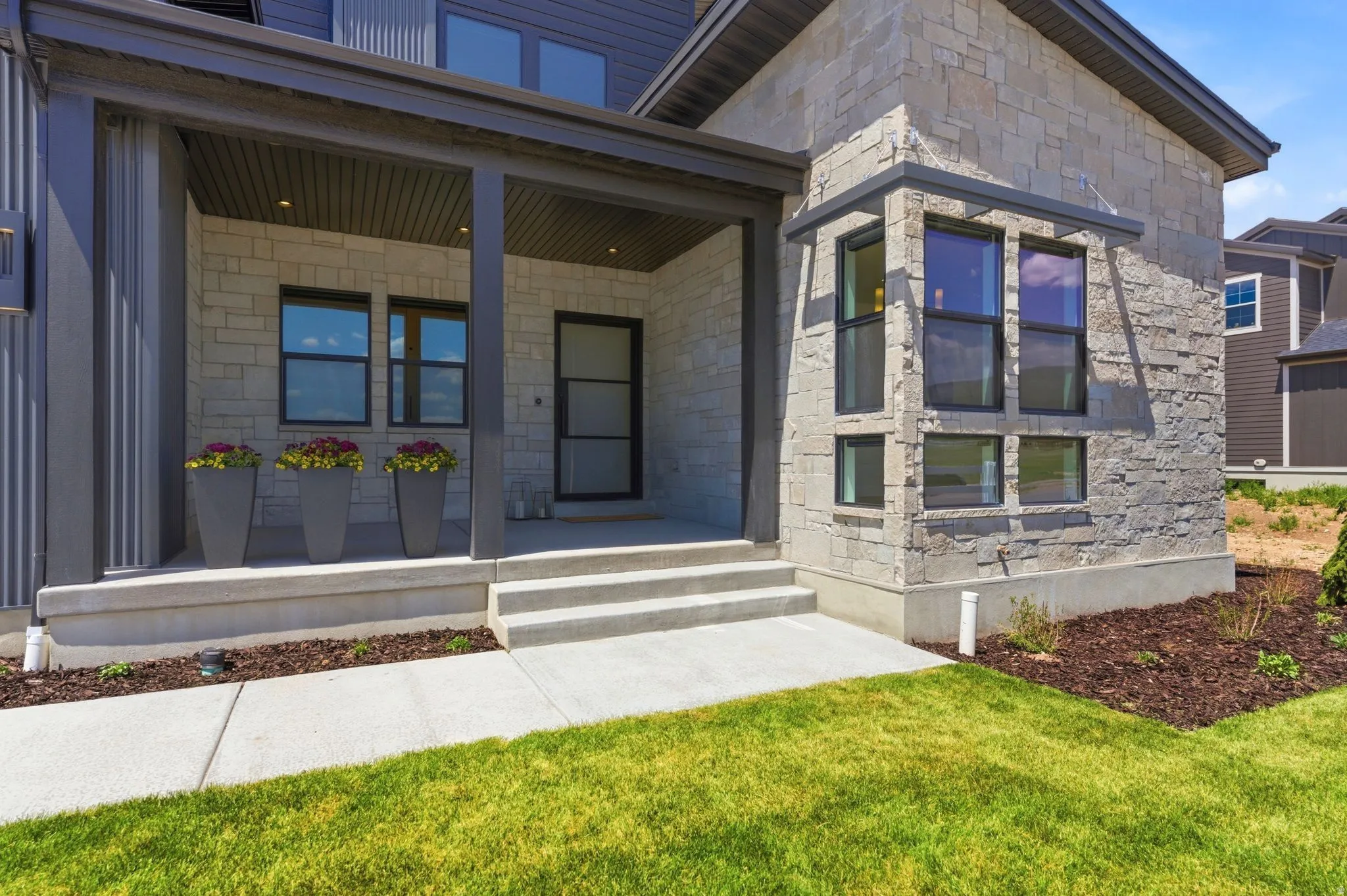 Modern exterior featuring a stone facade, covered porch entry, dark trim, and multiple window configurations