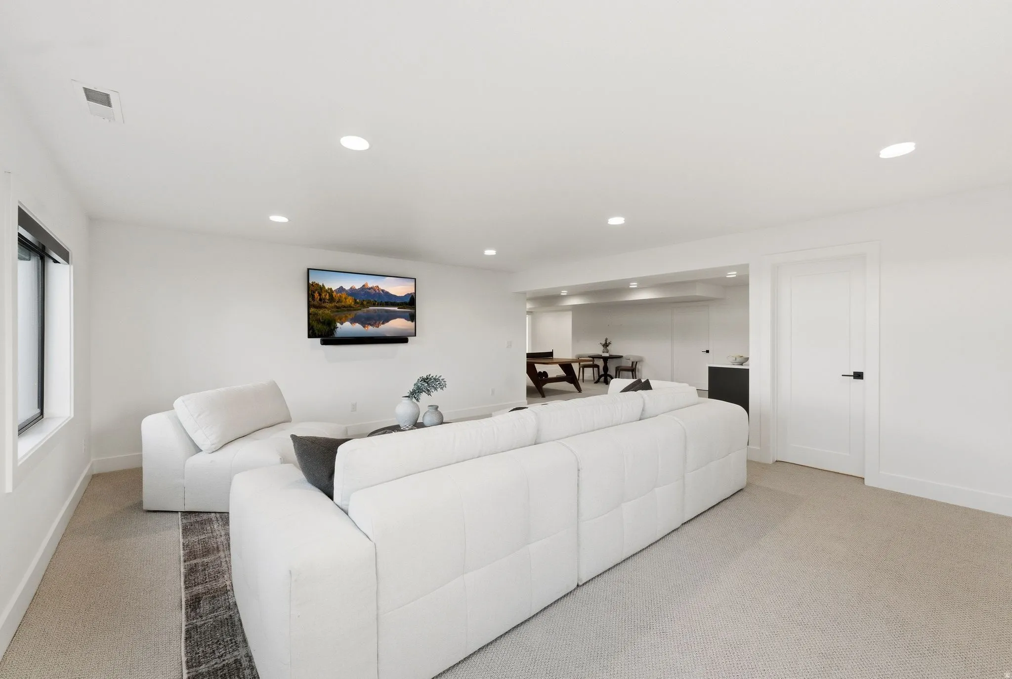 Spacious recreation room featuring recessed lighting, a mounted media display, neutral carpeting, and a white paneled interior door with matte black hardware