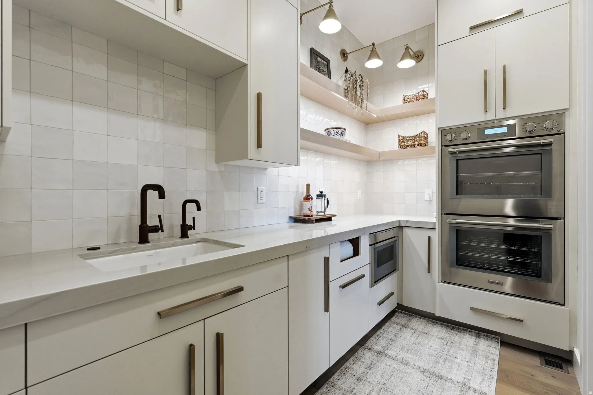 Modern kitchen featuring a built-in sink with matte black fixtures, crisp white cabinetry with bronze hardware, and a white square-tiled backsplash