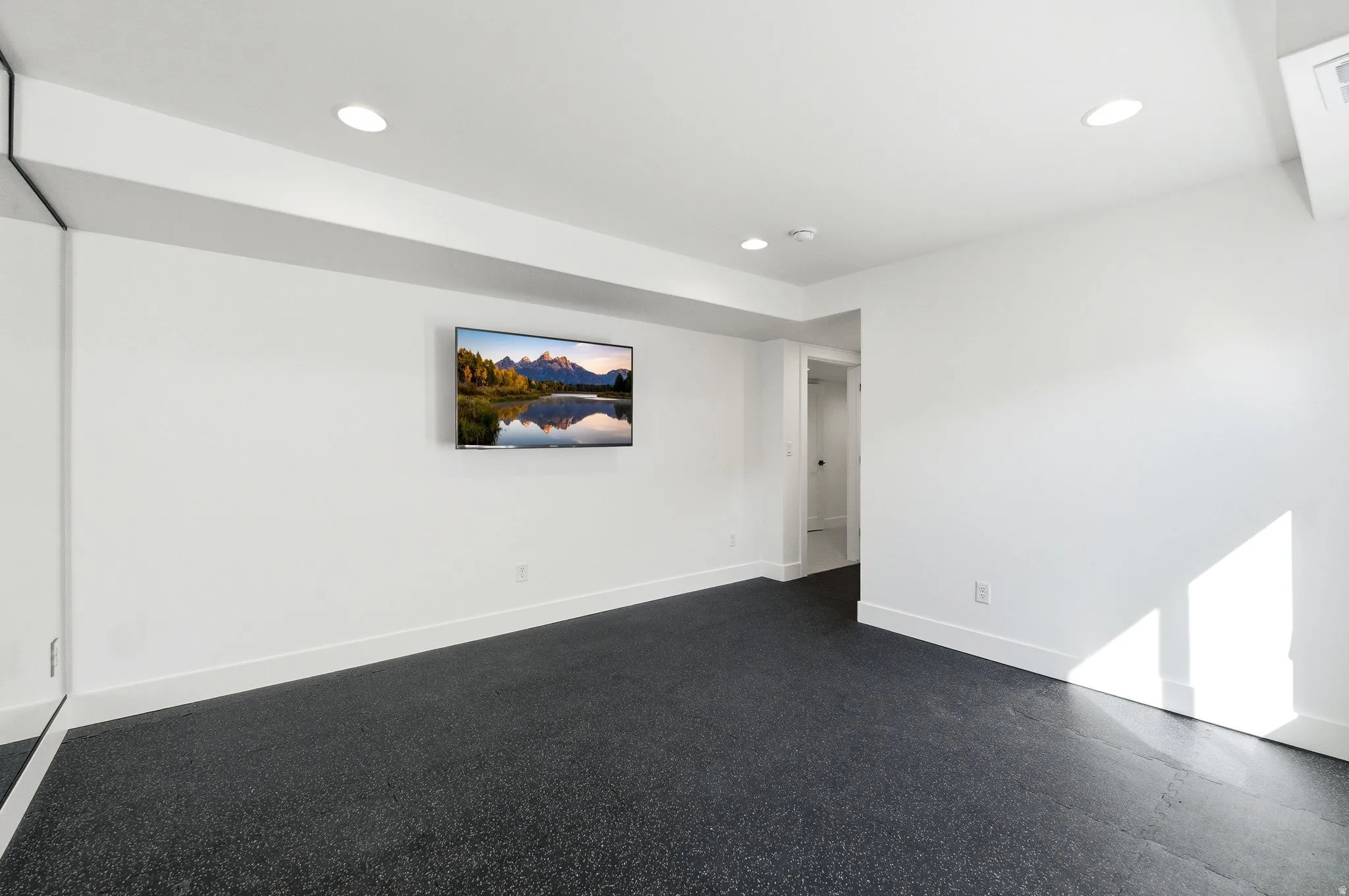 Spacious room featuring dark rubber flooring, white baseboards, recessed lighting, and a large wall-mounted mirror