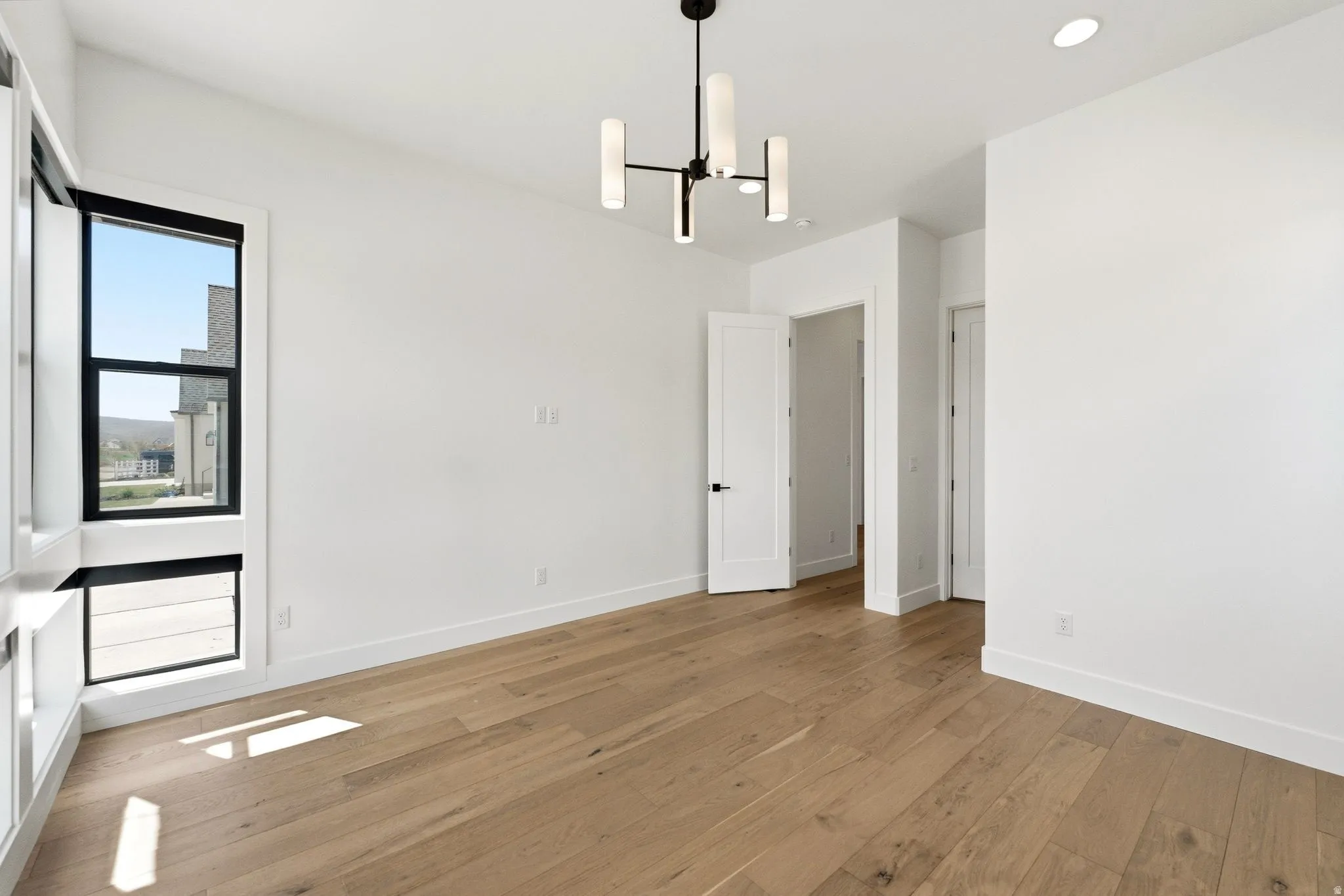Room featuring wood-finish flooring, white walls, and a contemporary chandelier