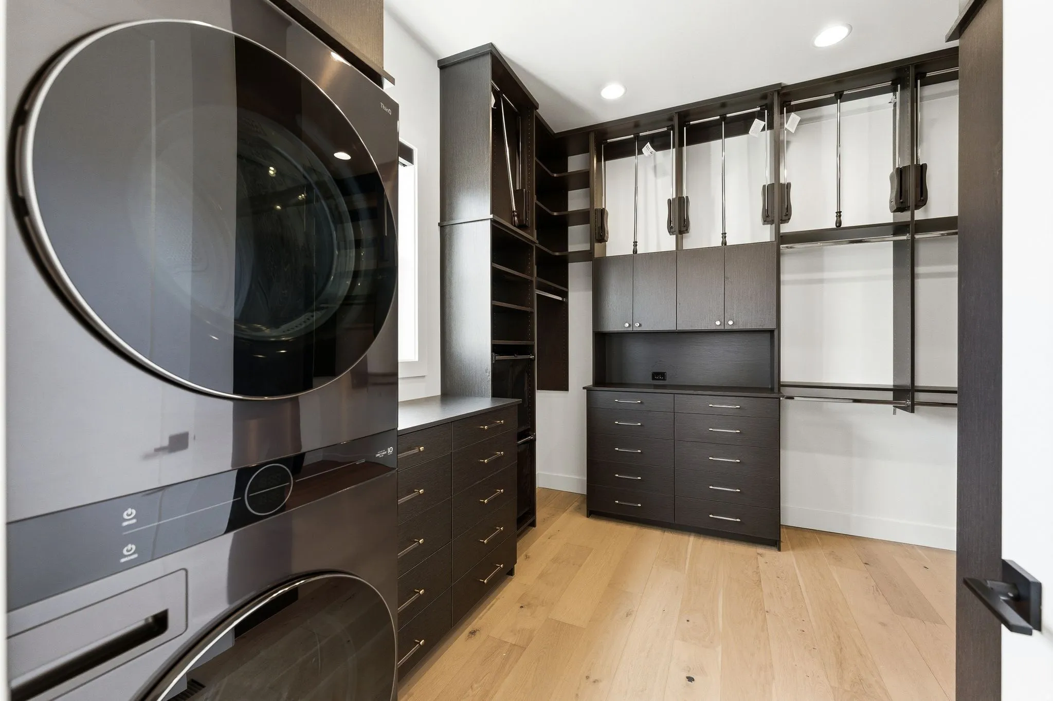 Custom closet system with light wood-finish flooring, dark wood-finish cabinetry, built-in shelving, and integrated washer and dryer units