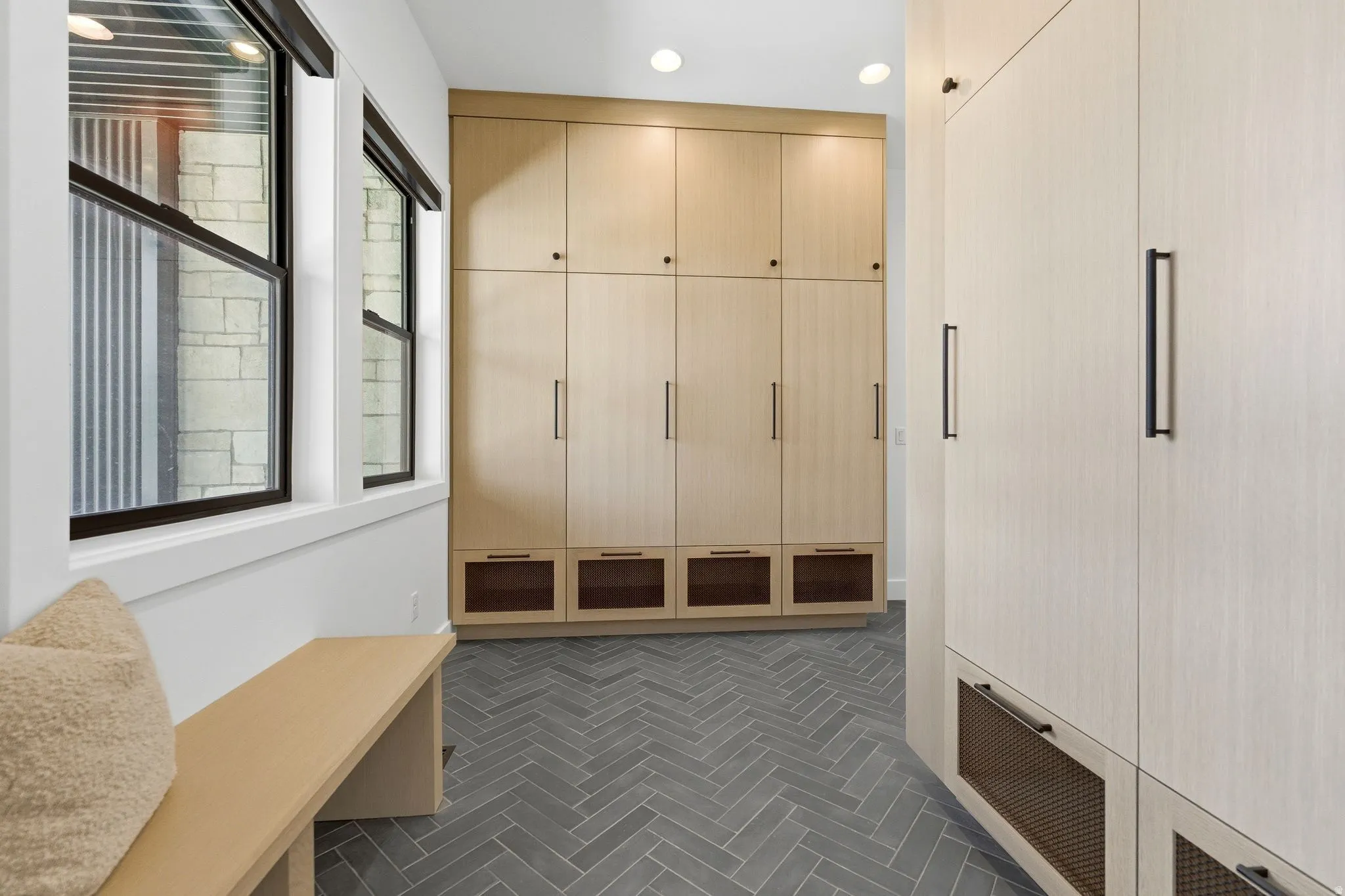 Hallway featuring extensive built-in cabinetry with modern hardware, grey herringbone-patterned tile flooring, a built-in bench, and multiple windows