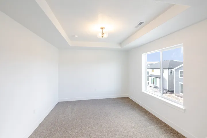 Recessed ceiling detail, contemporary flush-mount light fixture, white walls, carpeted flooring, and a large window