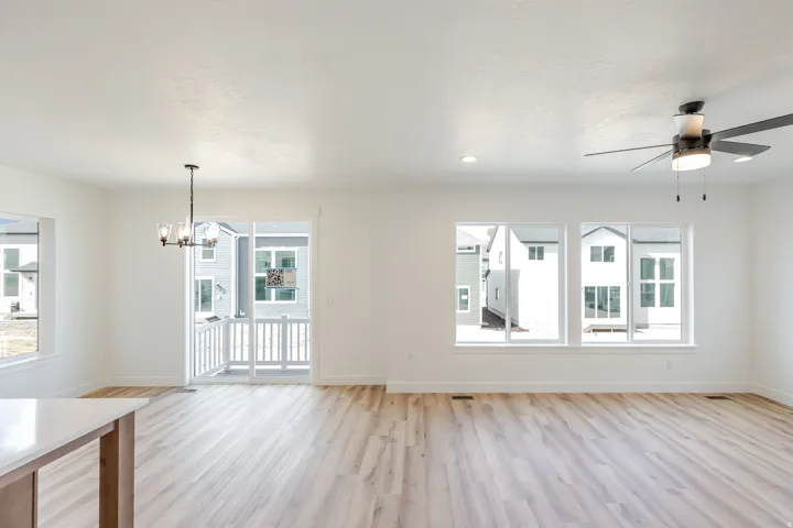 Light wood-finish flooring throughout, white walls, multiple large windows, recessed lighting, and a ceiling fan with integrated lighting