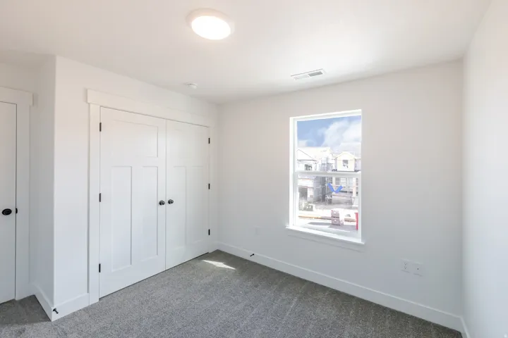 White double-door closet with dark hardware, gray carpet flooring, and a single window with white trim