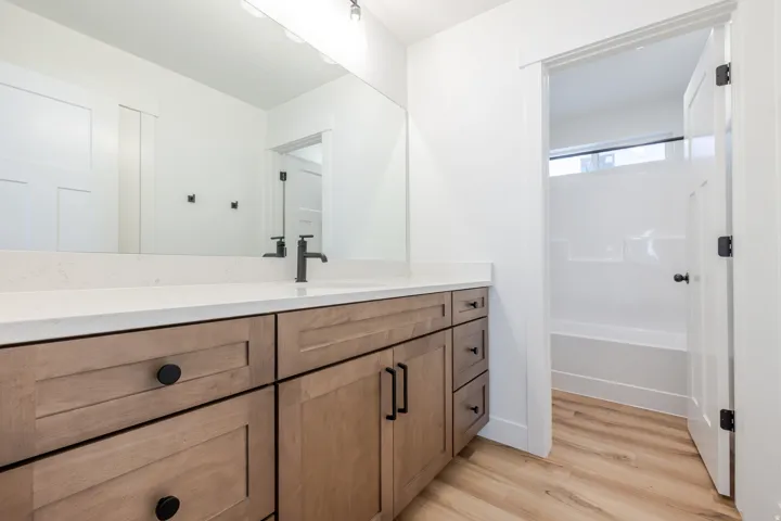 Double vanity with wood-finish cabinetry, white countertop, and matte black fixtures