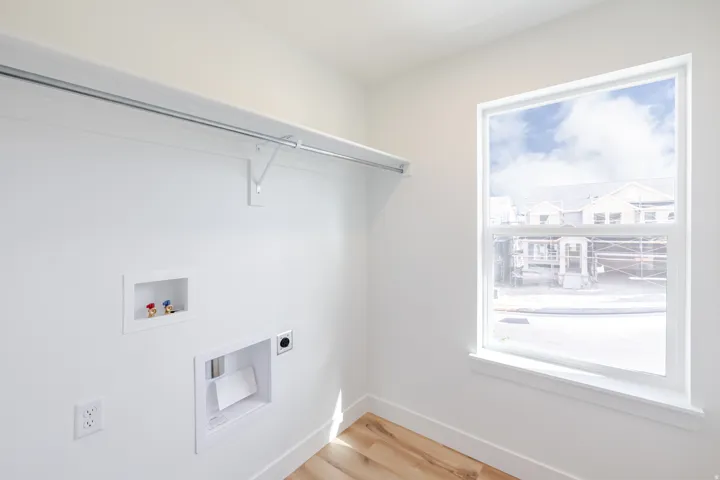 Dedicated laundry area featuring a utility sink connection, clothes dryer hookup, overhead hanging rod, and wood-finish flooring