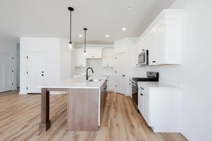 Kitchen featuring white cabinetry, a gas range, built-in microwave, a central island with a sink, and wood-finish flooring