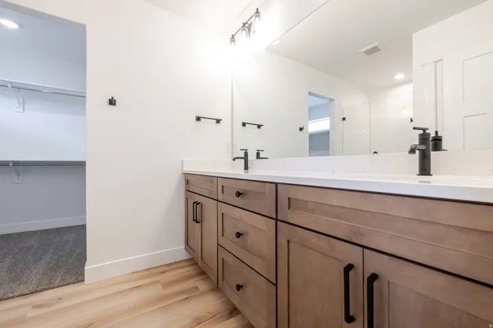 Double vanity with light wood-finish cabinetry, quartz countertops, and matte black fixtures