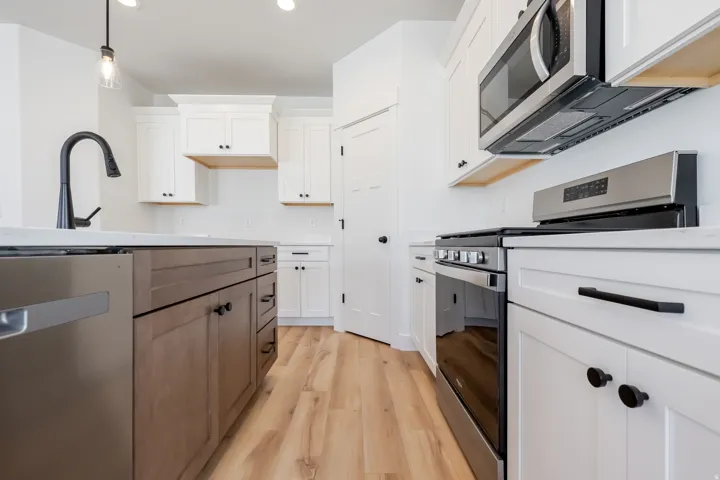 Kitchen featuring stainless steel appliances, wood-finish flooring, white cabinetry, a two-tone island, and matte black hardware