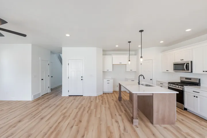 Open-concept living area featuring wood-finish flooring, white cabinetry, a kitchen island with seating, pendant lighting, and stainless steel appliances