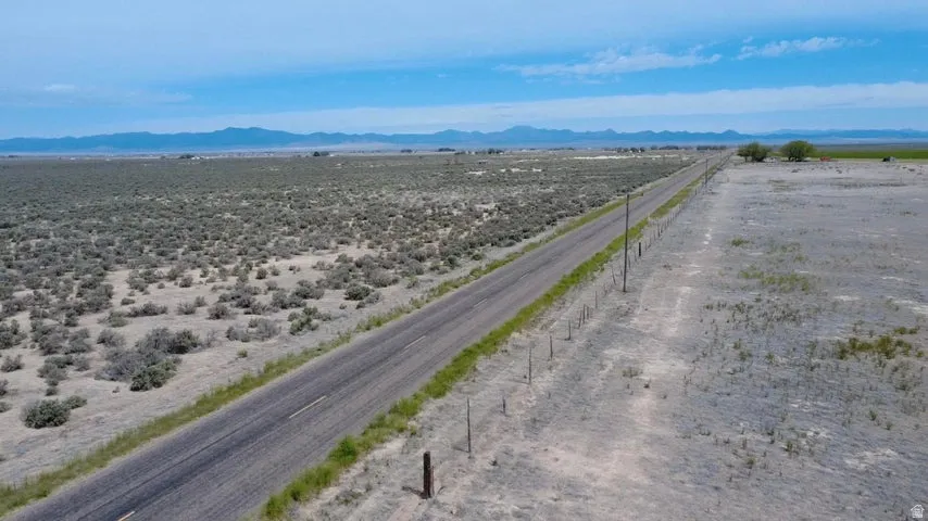 Expansive arid landscape featuring a paved road, scattered vegetation, and distant mountains under a blue sky