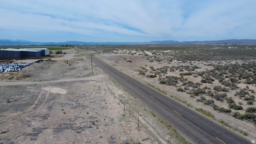 Expansive land parcel featuring an asphalt road, utility poles, and distant mountainous terrain