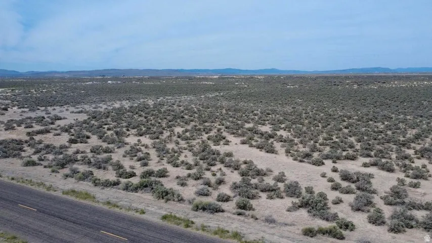 Expansive undeveloped land featuring arid ground cover and a paved road frontage