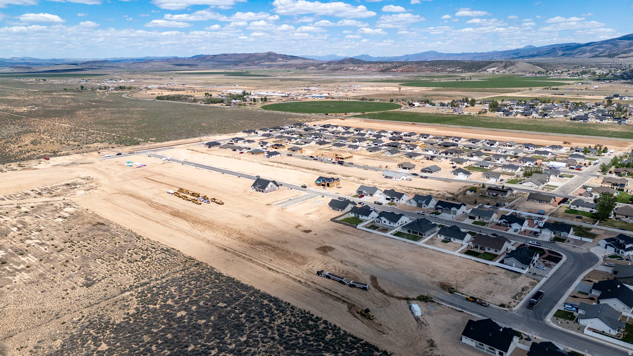 Expansive residential development featuring multiple completed homes, new construction sites, paved roads, and extensive undeveloped land with mountainous backdrops