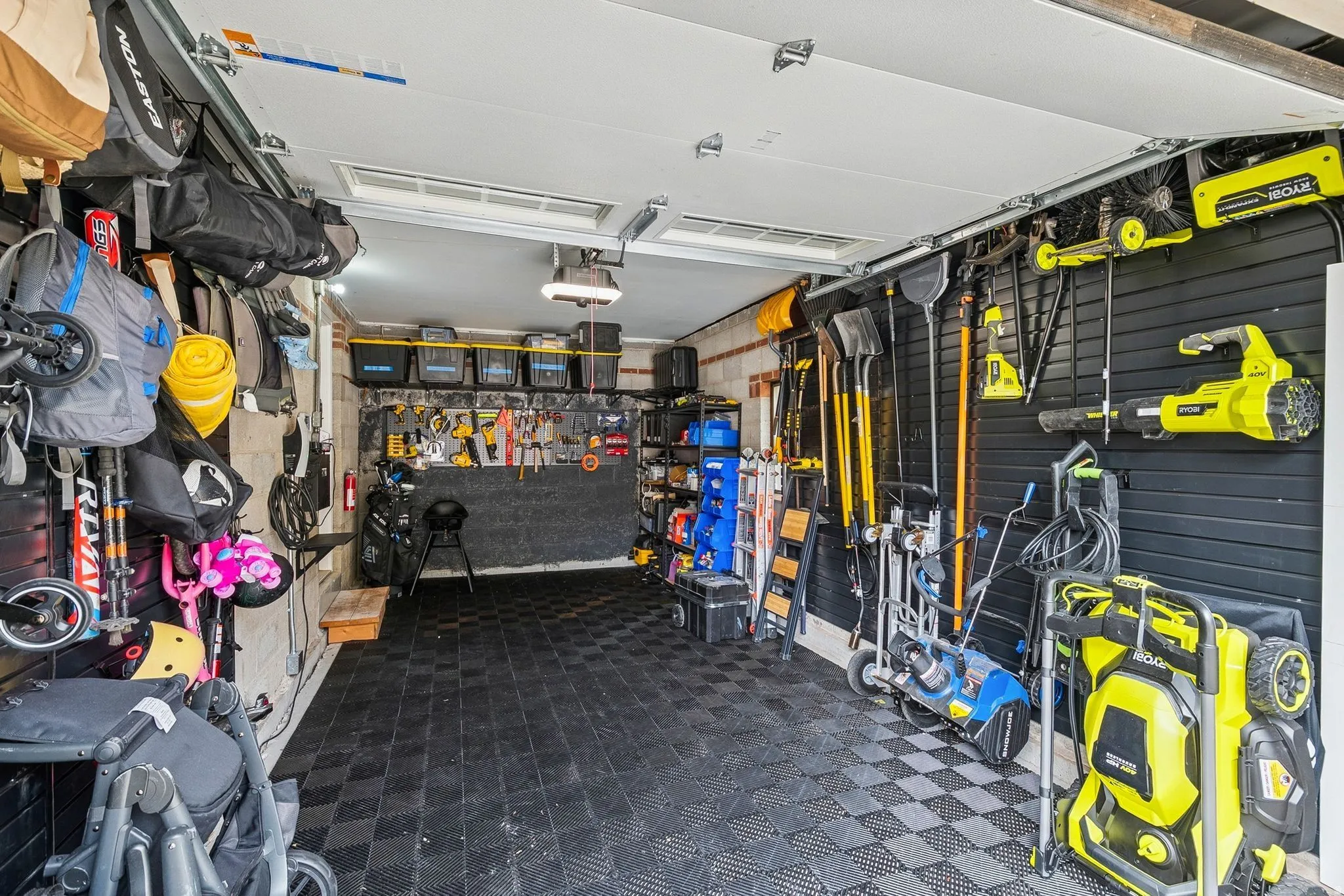 Garage space featuring checkerboard pattern flooring, slatwall organization systems, overhead lighting, and built-in shelving
