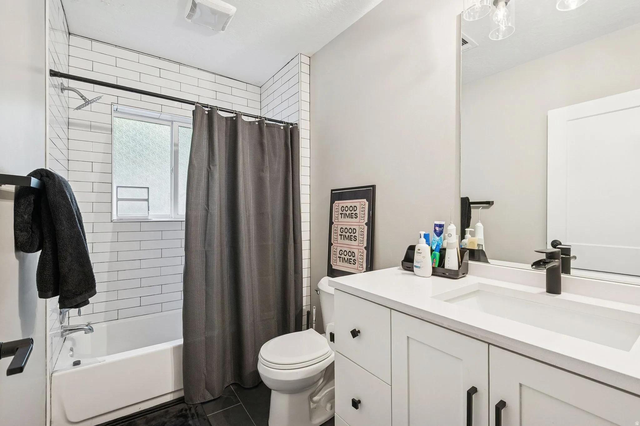 Bathroom featuring a white subway tile shower surround with a window, a white vanity with an integrated sink, a large wall-mounted mirror, and black hardware