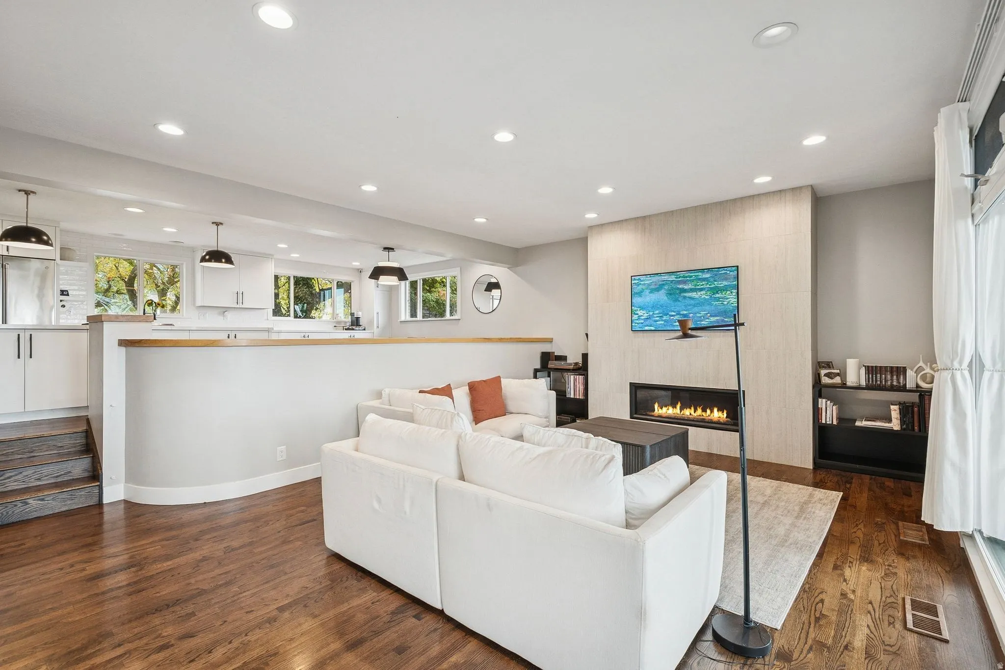Open-concept living area featuring rich wood-finish flooring, a contemporary linear fireplace with a textured tile surround, and recessed lighting