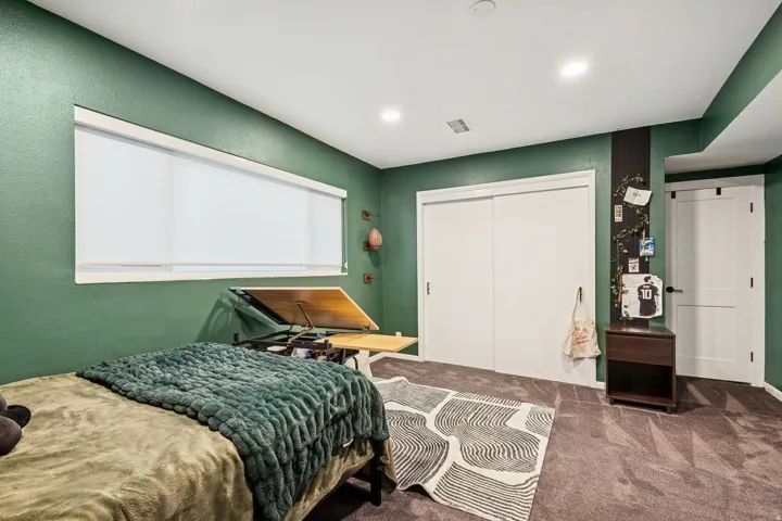 Carpeted room with a wide window featuring roller shades, built-in recessed lighting, and a two-panel sliding closet door