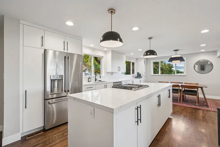 Modern kitchen featuring a large central island with a built-in gas cooktop, white perimeter cabinetry, stainless steel refrigerator, and wood-finish flooring