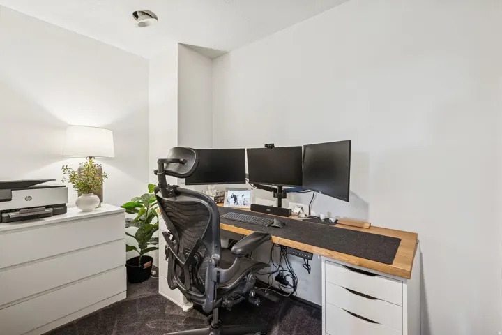 Dedicated workspace featuring a wood-finish desk surface, white storage units, and soft carpet flooring