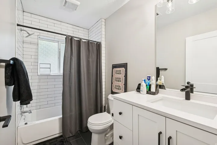 Bathroom featuring a white subway tile shower surround with a window, a white vanity with an integrated sink, a large wall-mounted mirror, and black hardware