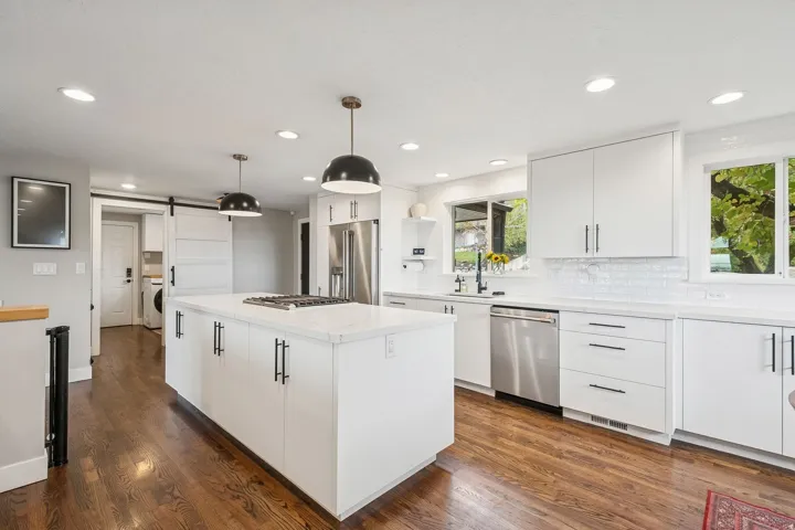Modern kitchen featuring a large central island with a cooktop, white cabinetry, stainless steel appliances, and wood-finish flooring