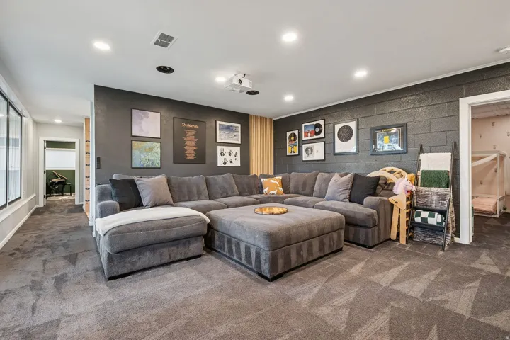 Carpeted recreation room featuring recessed lighting, a built-in projector, dark accent walls, and a large window providing ambient light