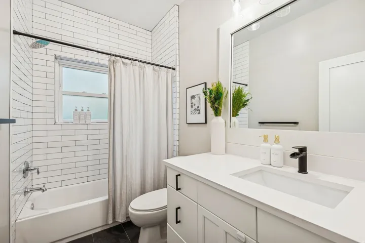 White subway tile surrounds the bathtub and shower combination, featuring a window and chrome fixtures