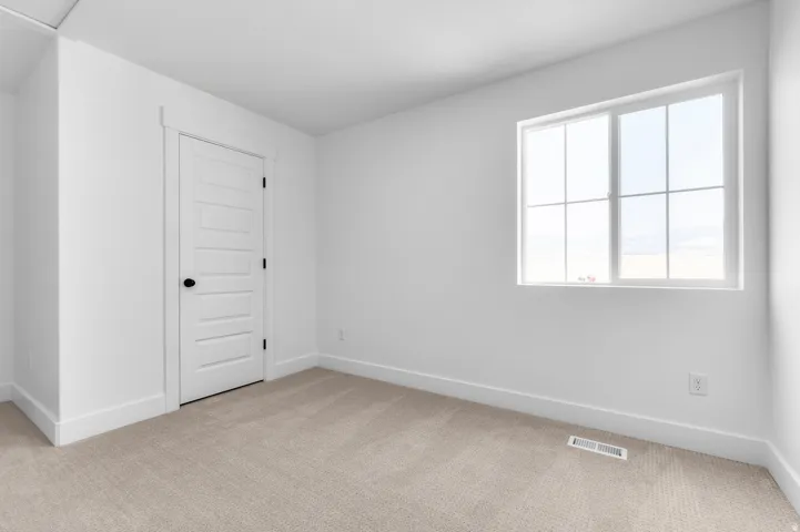 Bright, naturally lit bedroom showcasing large multi-pane window, neutral wall finishes, and soft-toned carpet flooring