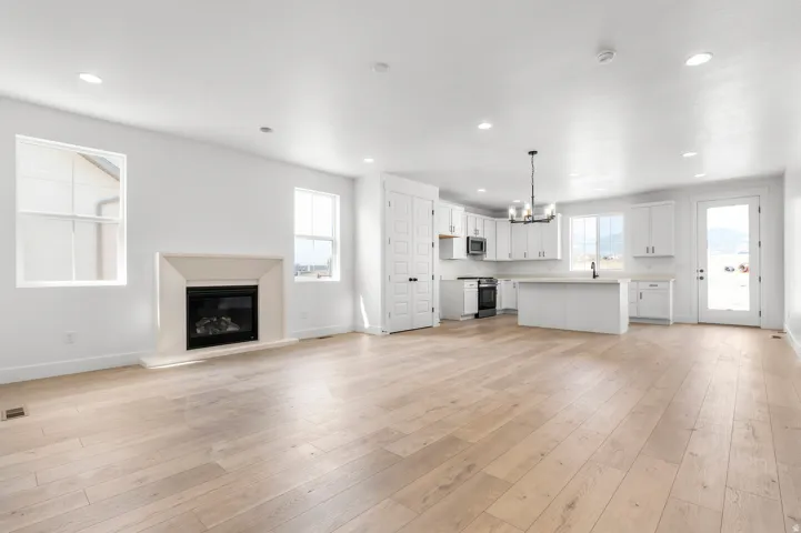 Open-concept living space showcasing gleaming wood-finish flooring throughout, a gas fireplace with a light-toned surround, recessed ceiling lighting, and abundant natural light from multiple windows