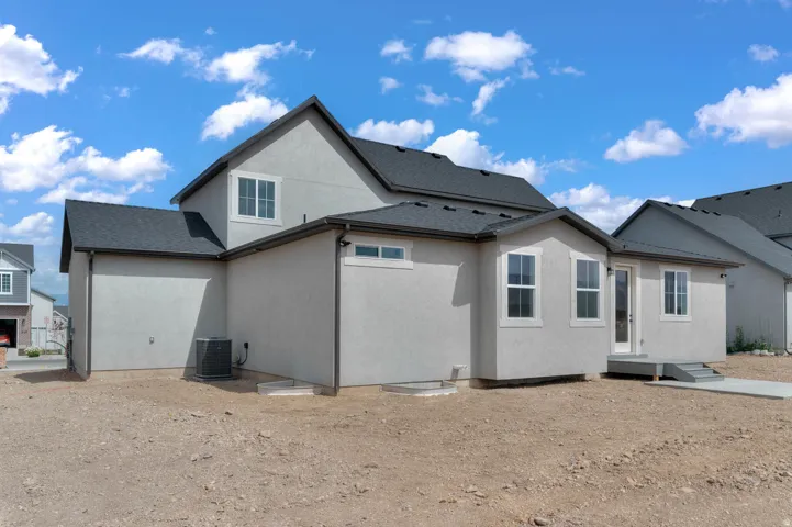 Stucco exterior with multiple windows, dark shingle roofing, and a rear patio door