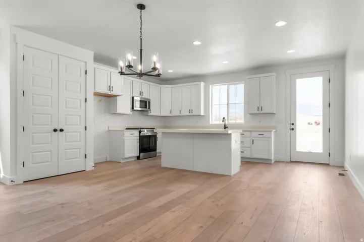 Bright, open kitchen featuring white cabinetry, stainless steel appliances, a large center island with seating, pendant lighting, and wood-finish flooring throughout