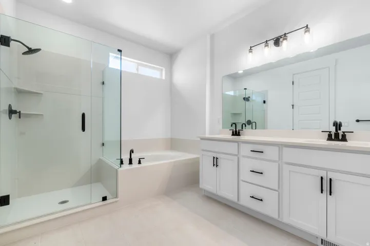 Spa-inspired primary bathroom featuring a freestanding soaking tub, dual-sink vanity with white cabinetry and brushed nickel hardware, quartz countertops, and a frameless glass-enclosed shower with rainfall showerhead and linear floor drain