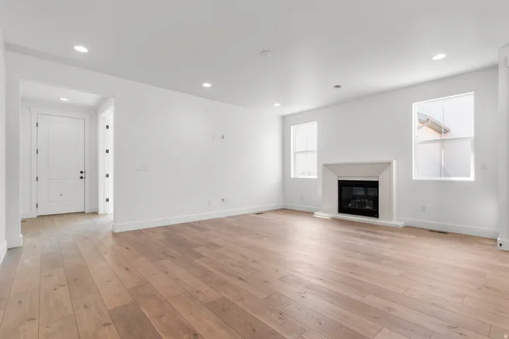 Spacious living area featuring wood-finish flooring, a contemporary fireplace with a light-toned surround, recessed lighting, and ample natural light from multiple windows
