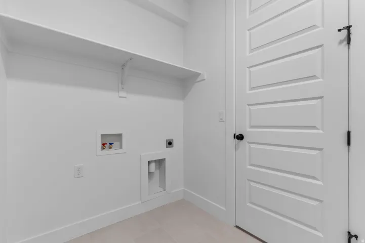 White wall-mounted shelving, laundry hookups, panel door with black hardware, and tiled flooring