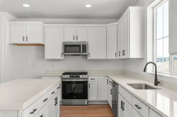 Contemporary kitchen featuring white shaker-style cabinetry with brushed nickel hardware, quartz countertops, stainless steel gas range with convection oven, and a matching stainless steel microwave