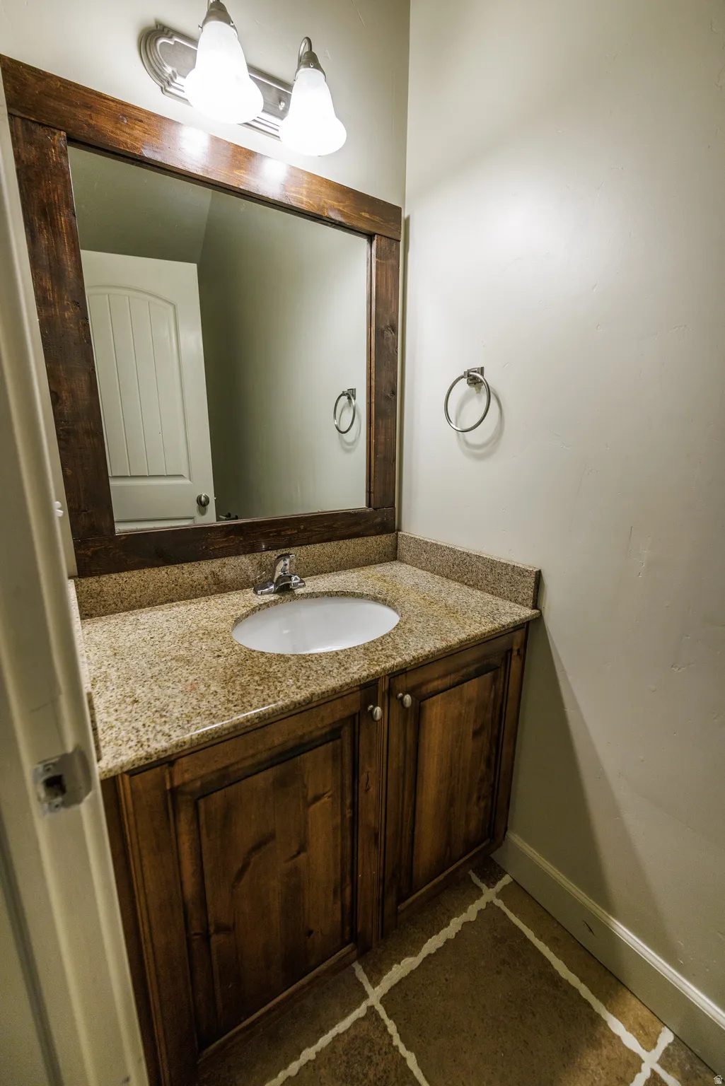 Bathroom vanity featuring wood-finish cabinetry, a granite-look countertop with an integrated sink, a wood-framed mirror, and a two-light vanity fixture