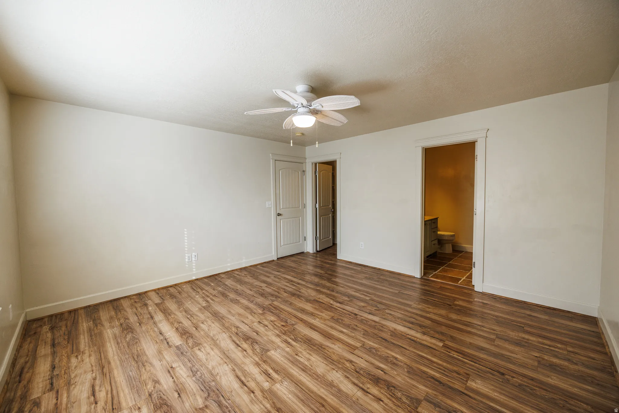 Spacious room featuring wood-finish flooring, white baseboards, and a ceiling fan with integrated lighting
