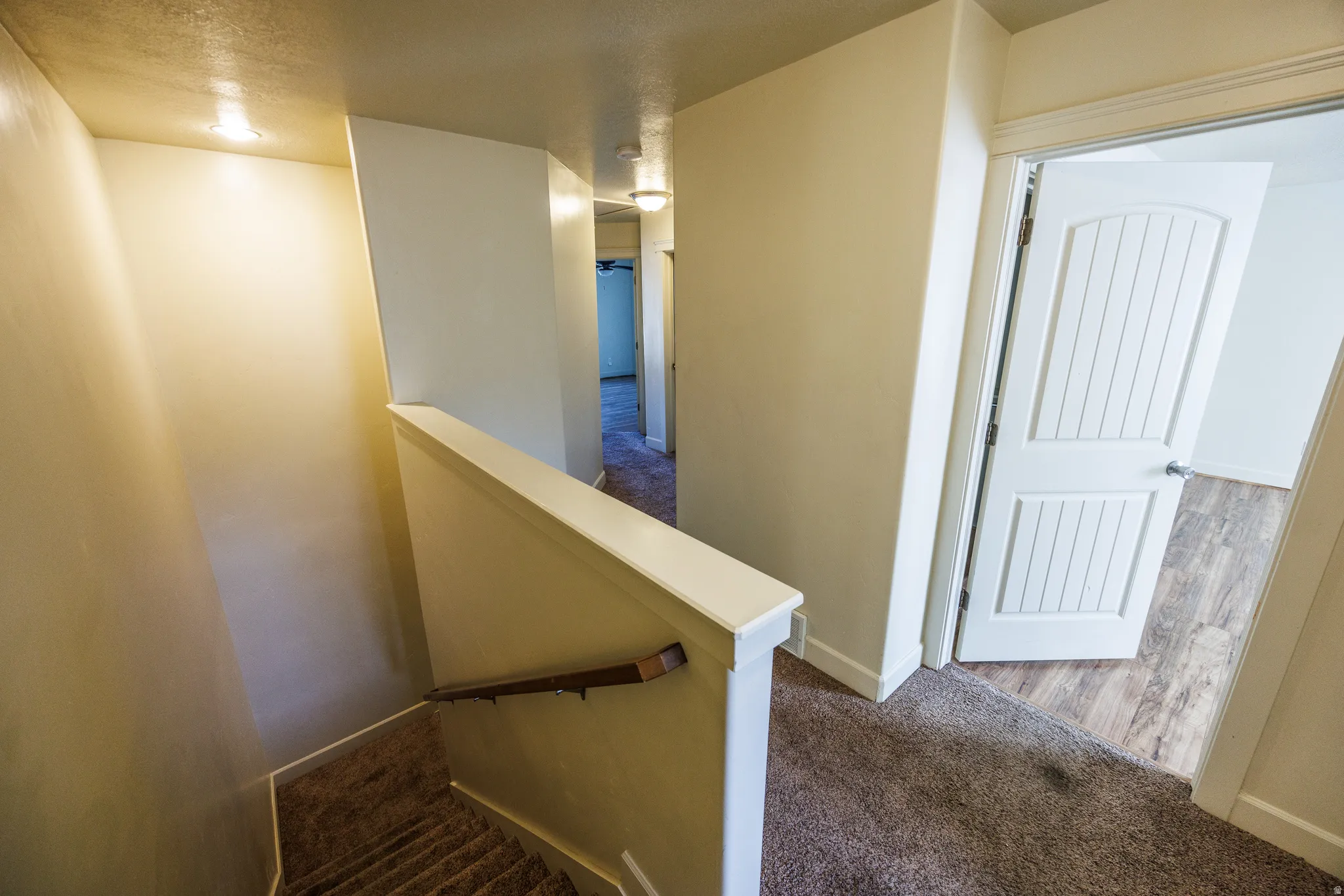Carpeted staircase featuring a wood handrail, white painted railing, and recessed ceiling lighting