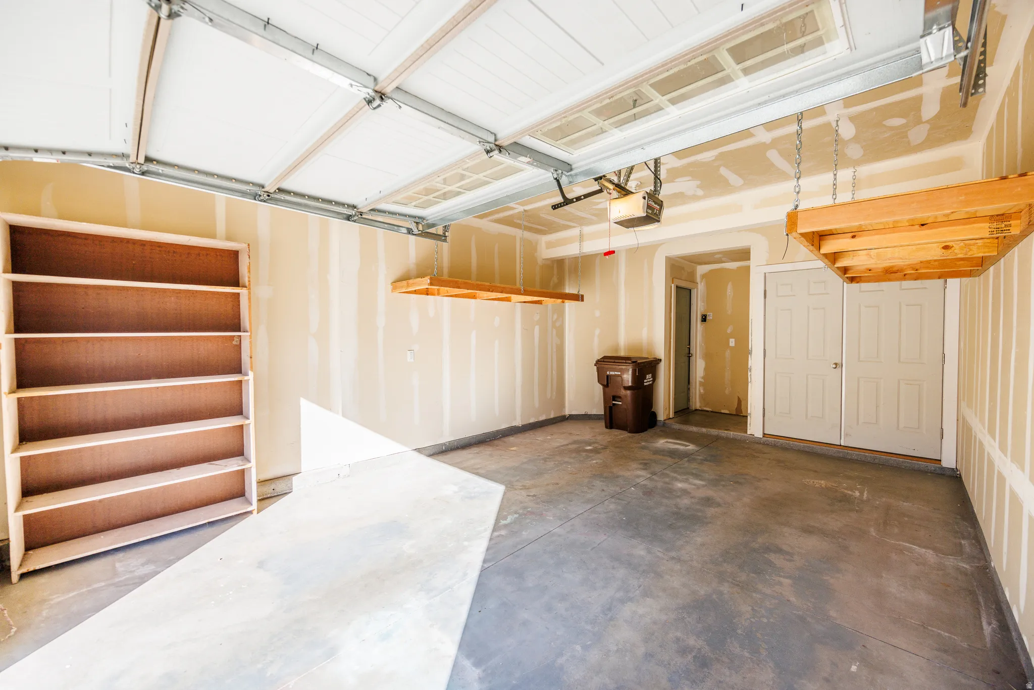 Spacious garage featuring a concrete floor, overhead garage door, built-in shelving, two overhead storage platforms, and interior access doors