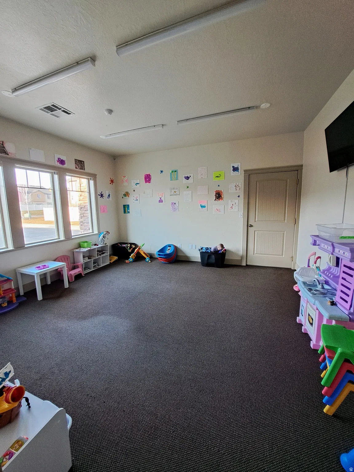 Spacious room featuring carpeting, multiple windows providing natural light, a neutral wall finish, and overhead strip lighting