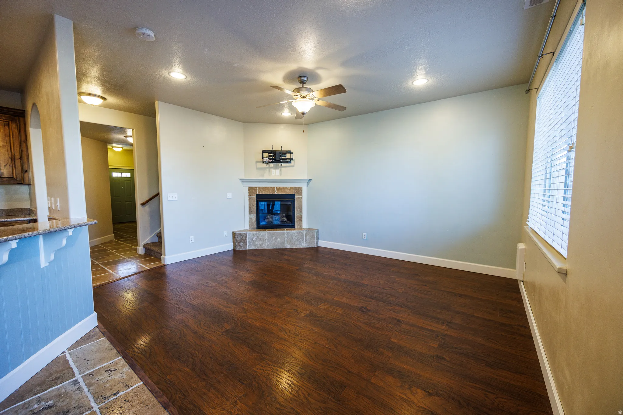 Spacious living area featuring wood-finish flooring, a corner fireplace with a tiled hearth and surround, and a ceiling fan