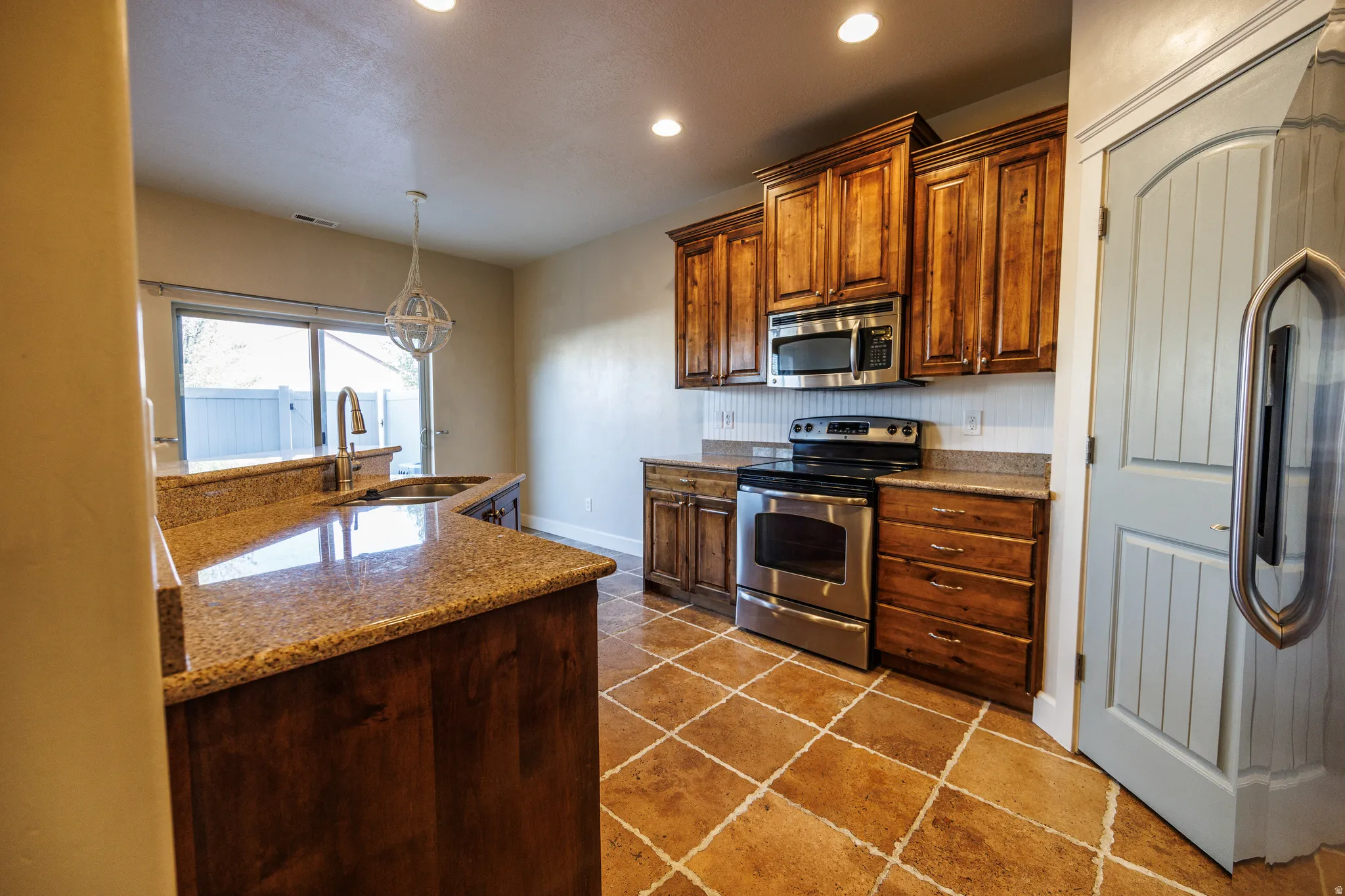 Kitchen featuring granite countertops, wood cabinetry, stainless steel appliances, and tiled flooring
