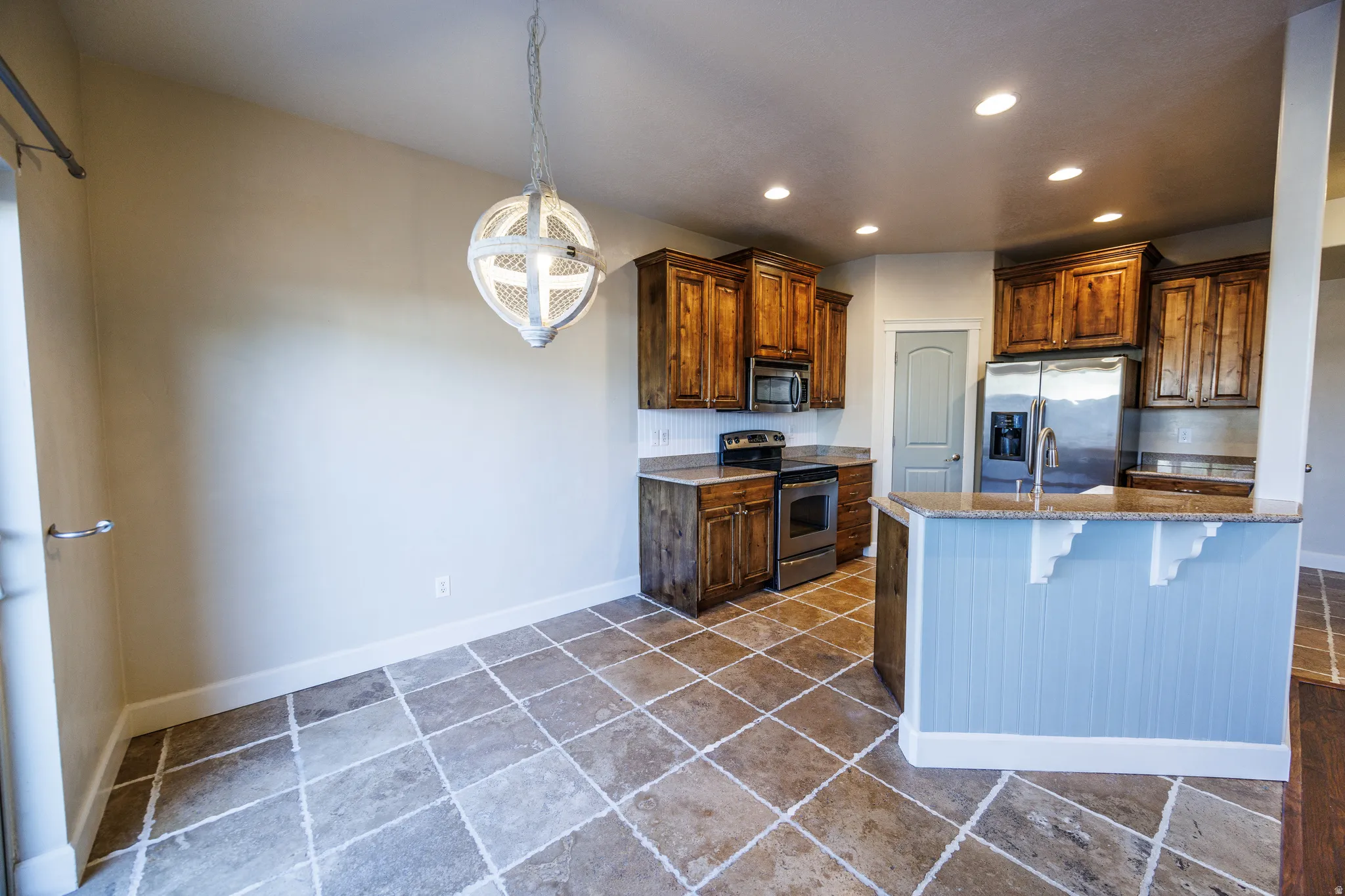 Kitchen and dining area featuring diagonal tile flooring, wood cabinetry, stainless steel appliances, a breakfast bar with beadboard paneling, and an orb pendant light fixture