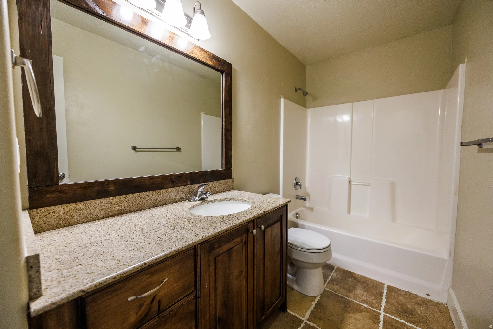 Bathroom featuring a wood-finish vanity with a light-colored countertop, an integrated sink, and a large framed mirror