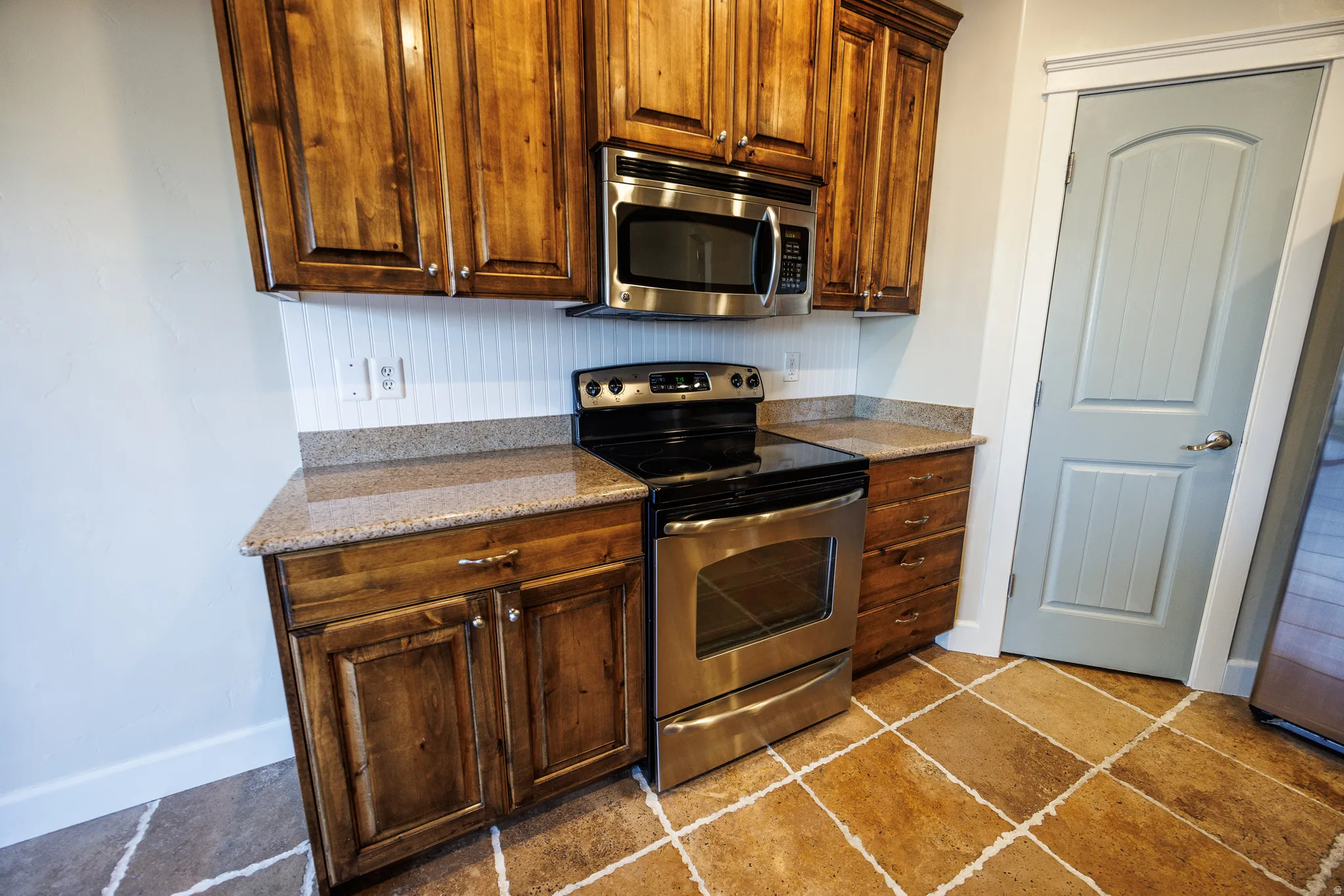 Kitchen featuring wood cabinetry, stainless steel microwave, stainless steel range, granite-finish countertops, and wood-finish flooring