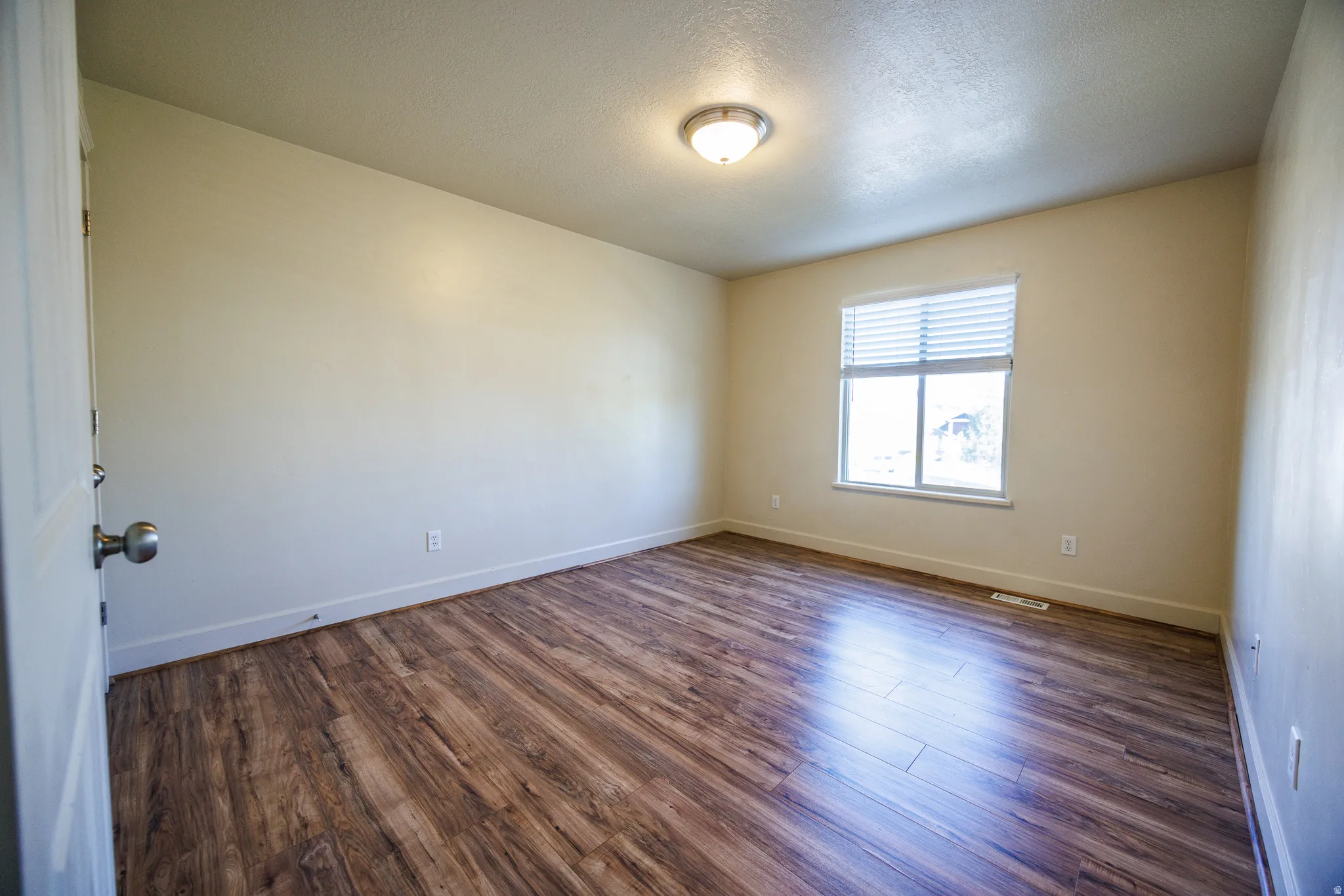 Room featuring wood-finish flooring, neutral wall tones, a flush-mount ceiling light fixture, and a window with horizontal blinds